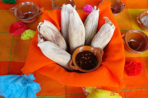 tamales de hoja de maiz, montados en una zanasta con un cuenco de slasa